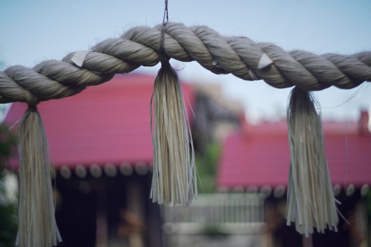 Плетёная священная верёвка и подвесы на фоне красной крыши. Япония.